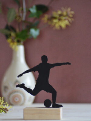 Silhouette en métal noir d'un footballeur en action, montée sur un socle en bois (10 cm x 13 cm). Une décoration élégante et moderne pour les passionnés de football.