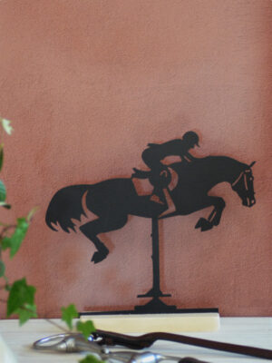 Silhouette en métal noir d’une cavalière et son cheval sautant un obstacle, montée sur un socle en bois. Une décoration élégante pour les passionnés d’équitation.